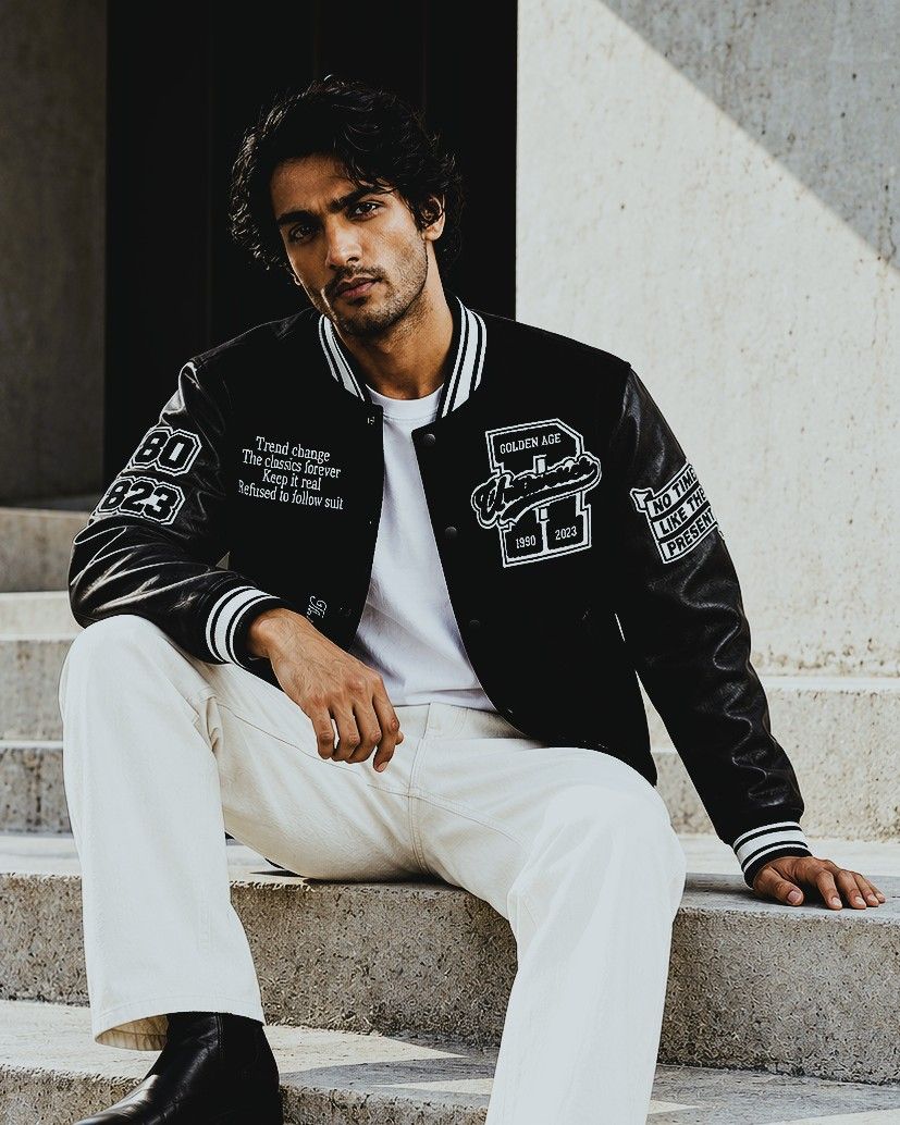 Model in a black varsity jacket sitting on stone steps
